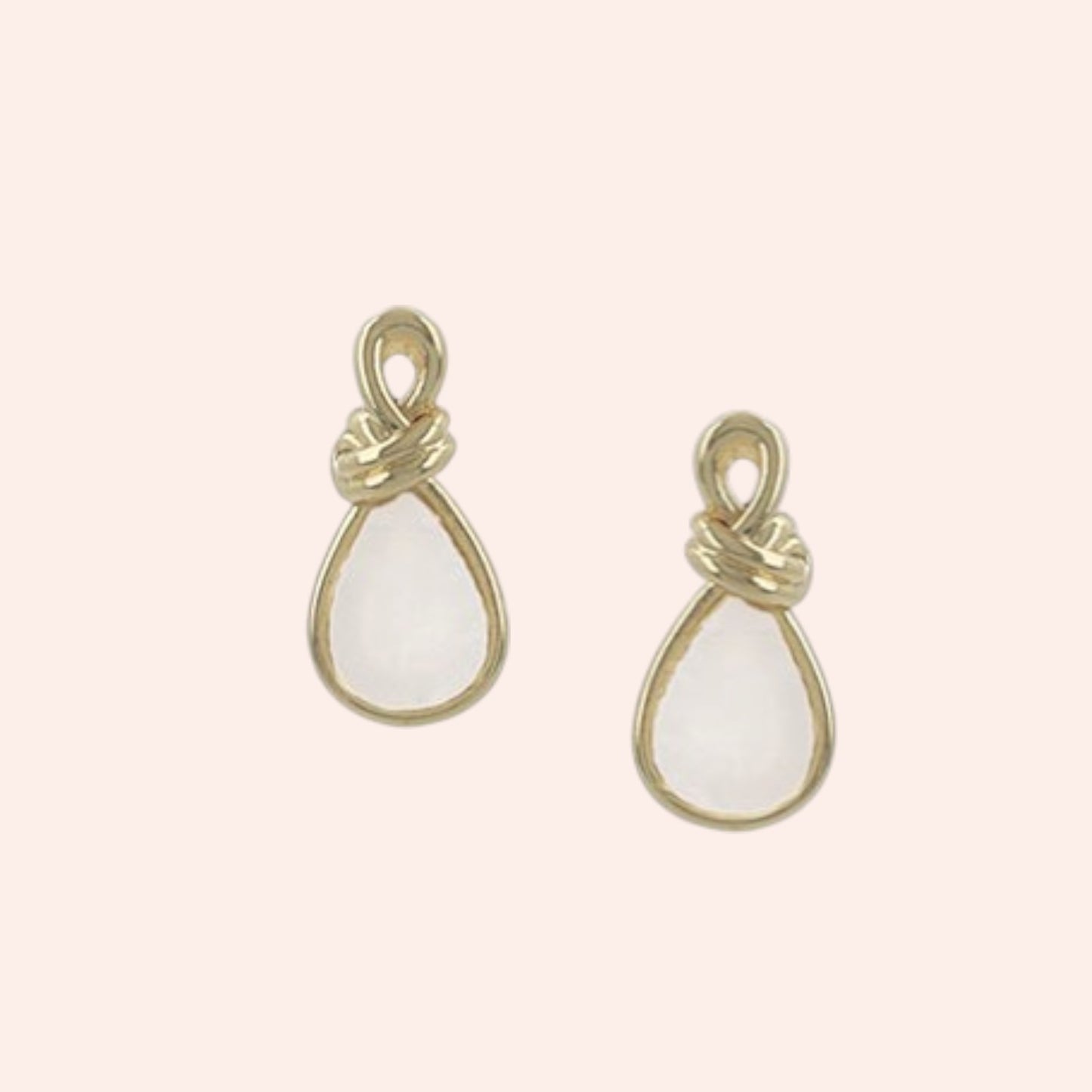 Gold teardrop-shaped earrings with white stones on a light pink background