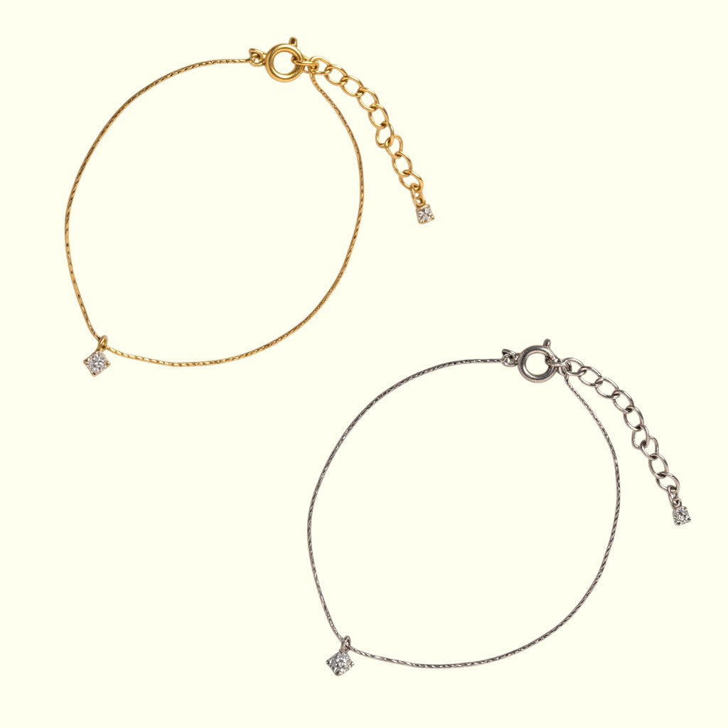Gold and silver anklets with small diamond-like pendants on a white background