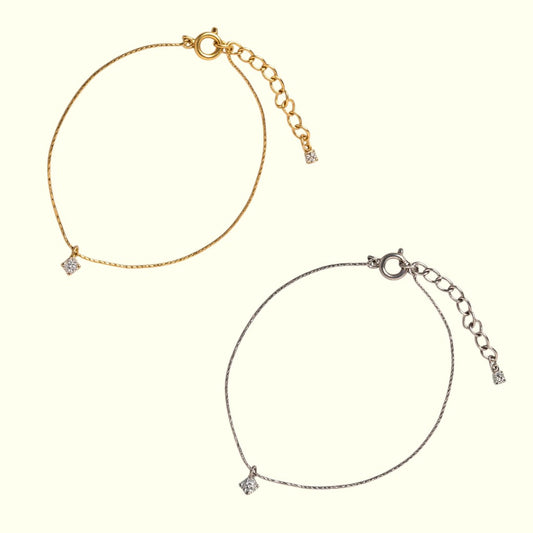 Gold and silver anklets with small diamond-like pendants on a white background