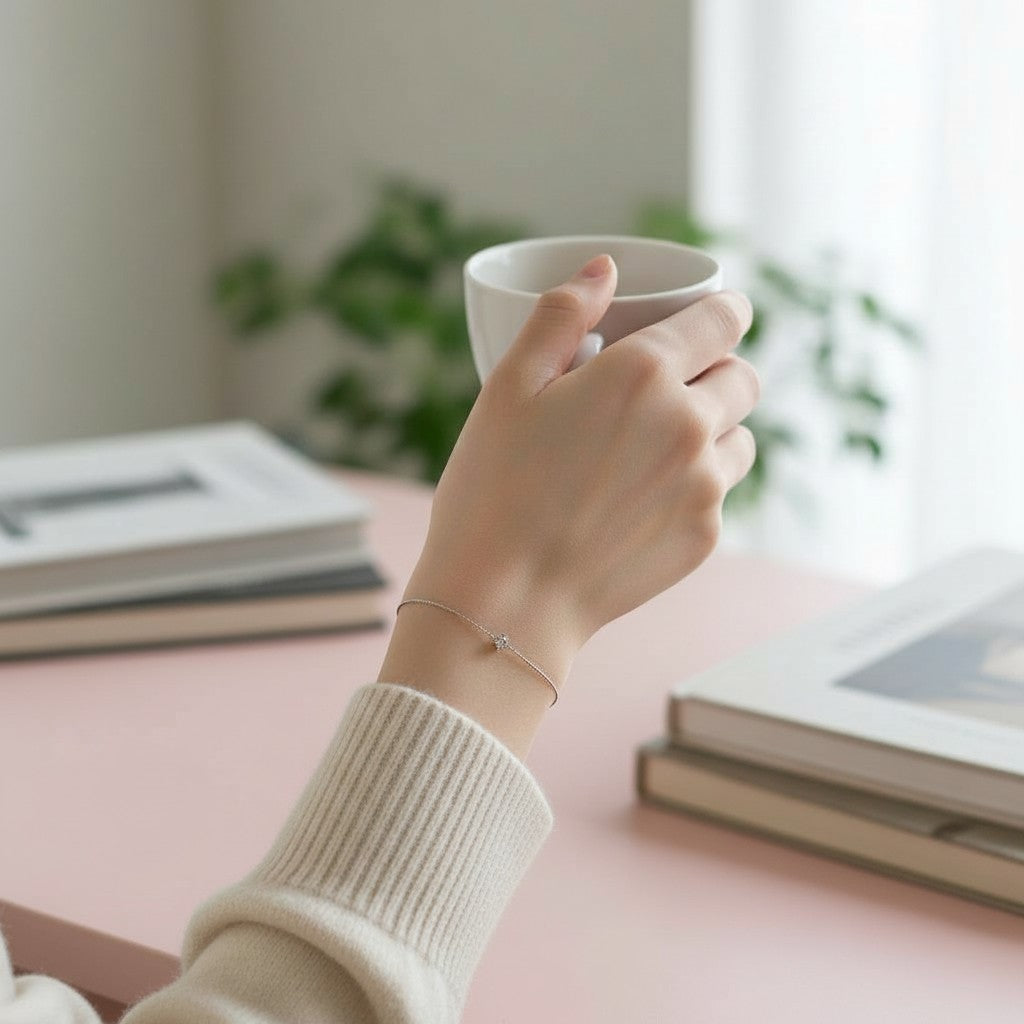 Hand wearing bows and knots co. Bracelet holding a white mug on a pink surface with books and plants in the background