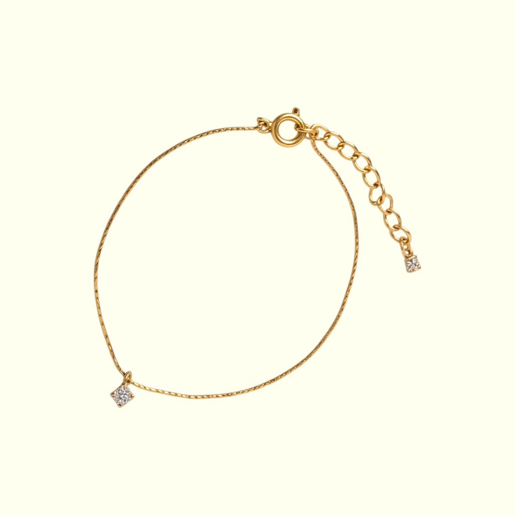 Gold bracelet with a small diamond charm on a beige background