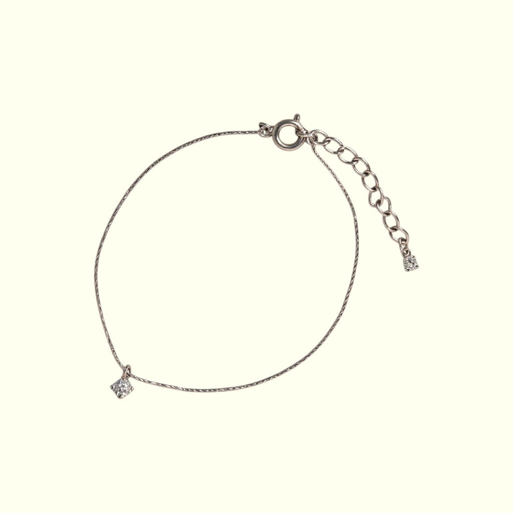 Silver bracelet with a small diamond on a beige background