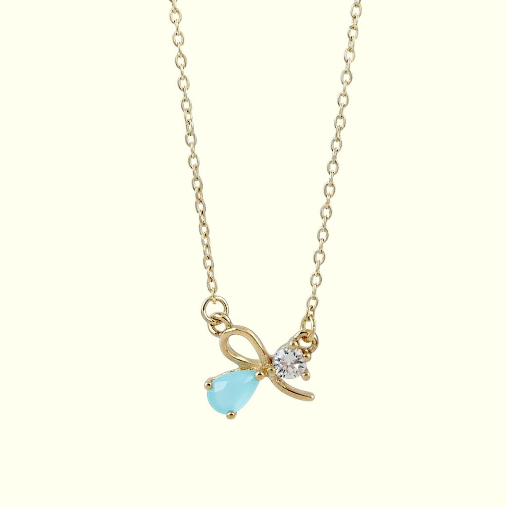 Gold necklace with a bow and blue teardrop pendant on a white background