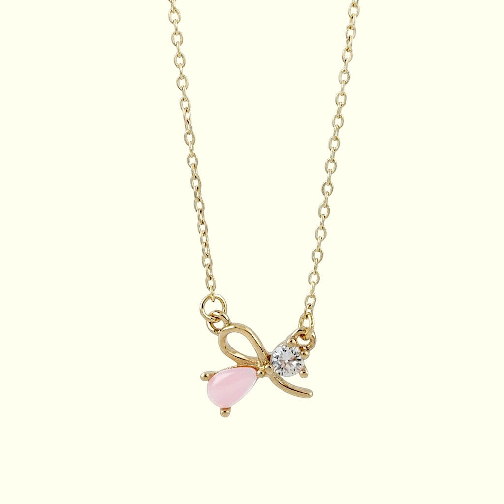 Gold necklace with a pink bow pendant on a white background