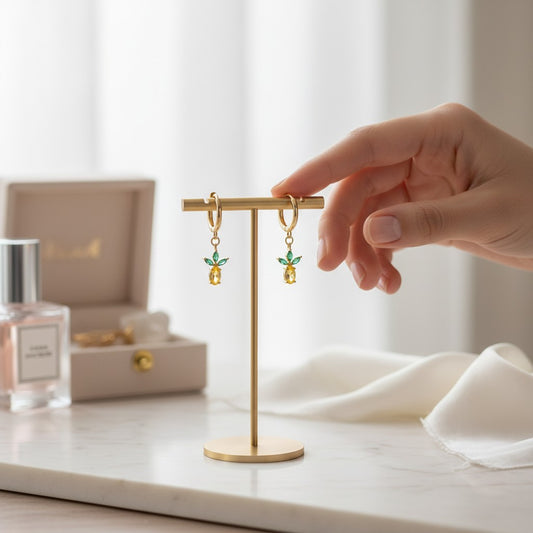 Gold earring stand with earrings on a marble surface, with a hand reaching towards it.