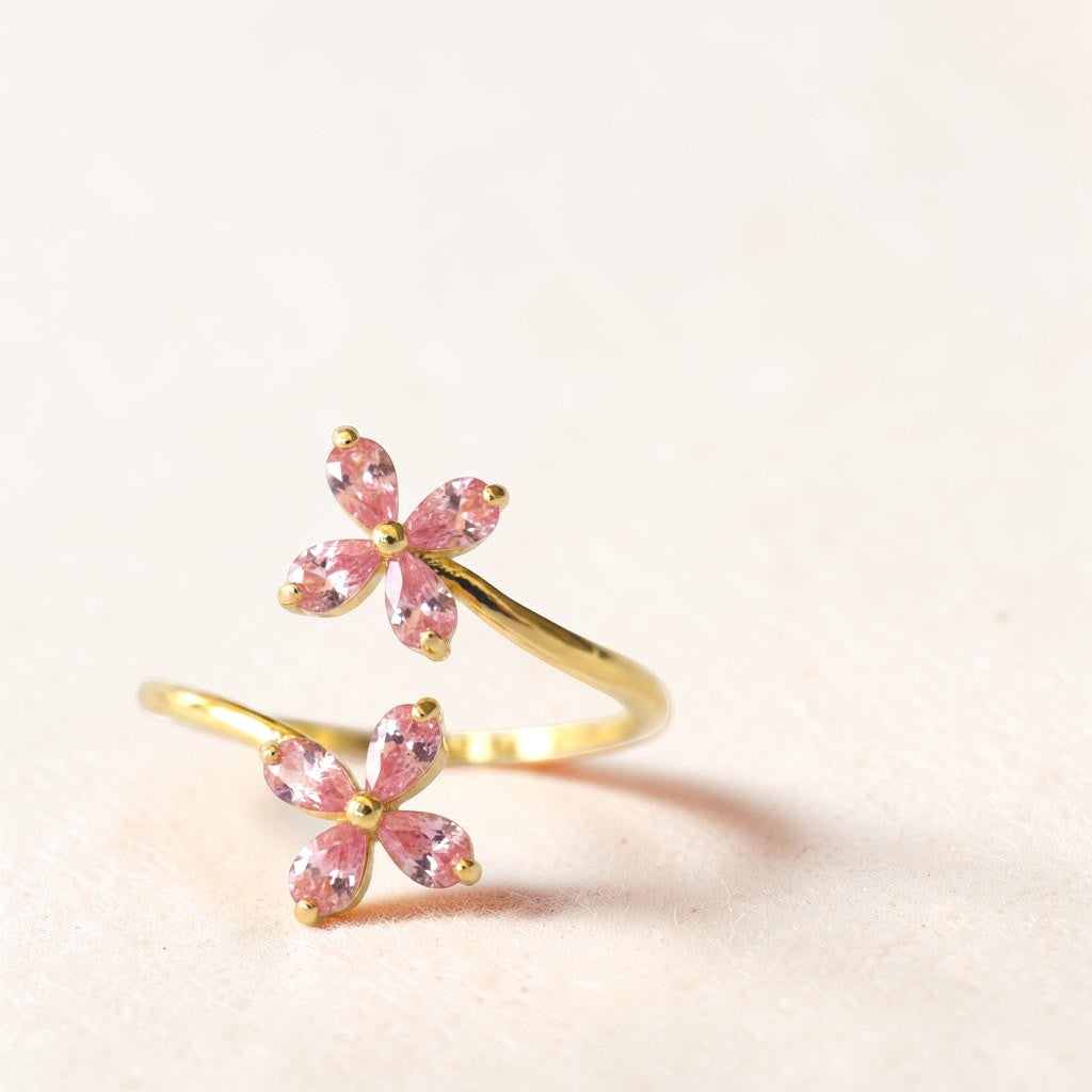 Gold ring with pink gemstone flowers on a light beige background