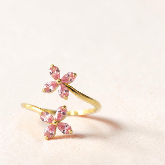 Gold ring with pink gemstone flowers on a light beige background
