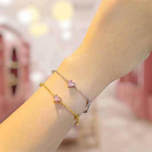 Gold and silver bracelet with pink heart charms on a wrist against a blurred background