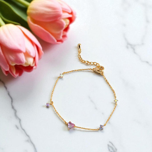 Gold bracelet with small stones on a marble surface with pink tulips