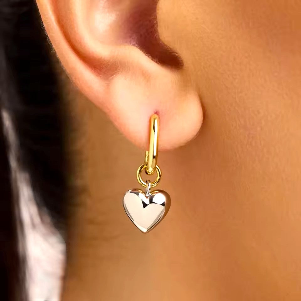 Gold heart-shaped earring worn on an ear with a blurred background