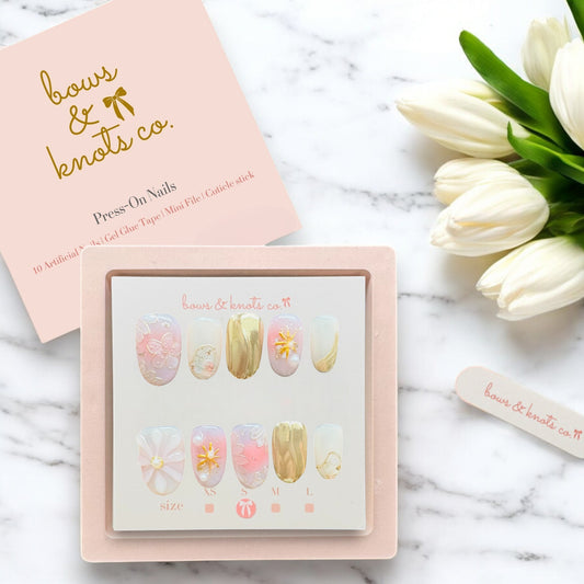 Set of press-on nails with a pink case on a marble surface with tulips.