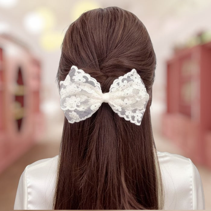 Person with long brown hair tied back with a decorative white lace bow.