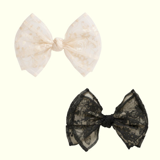 Two hair bows, one white with gold pattern and one black lace, on a white background.