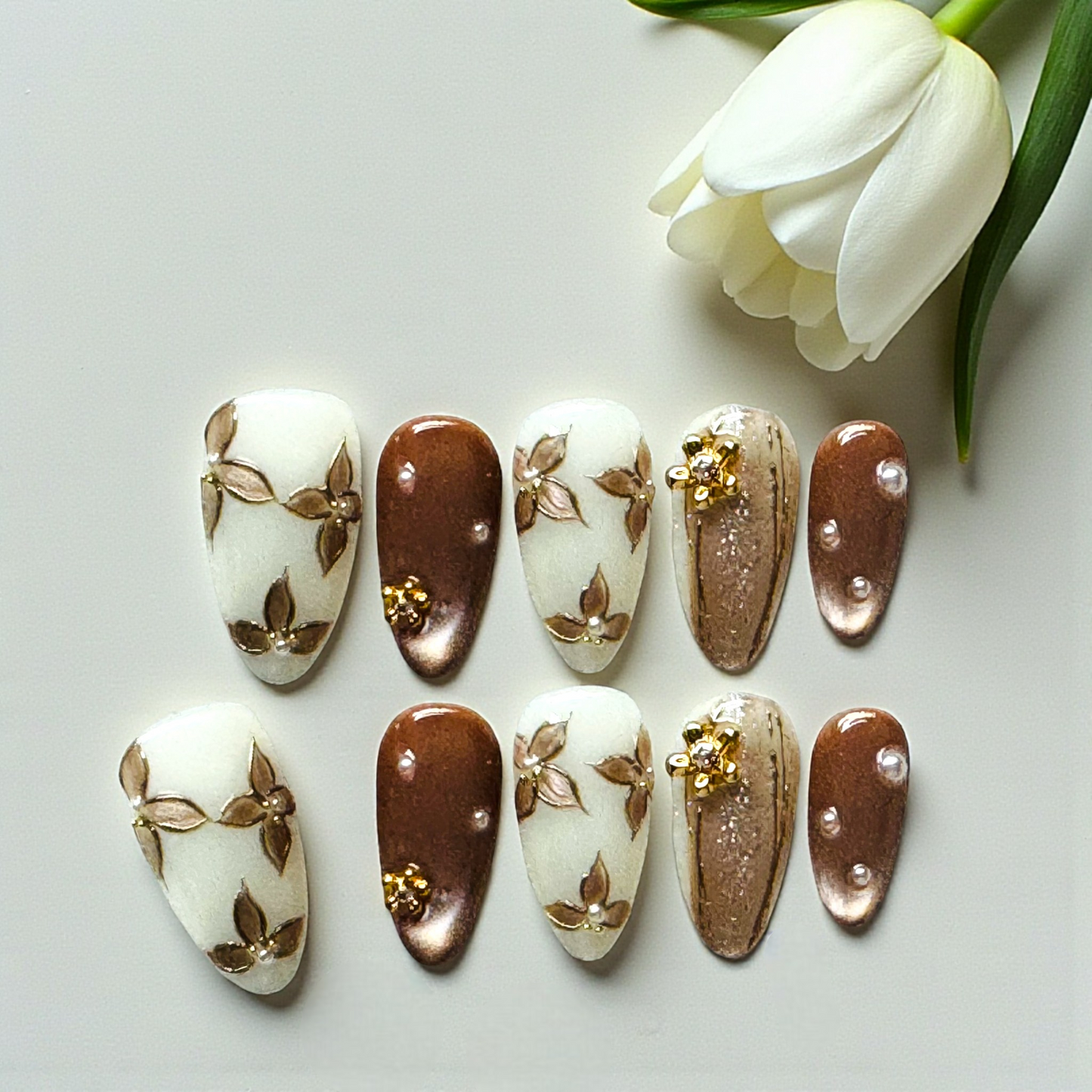 Set of nail art designs on a white surface with a white tulip.