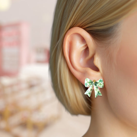Green bow-shaped earrings worn by a person with a blurred background