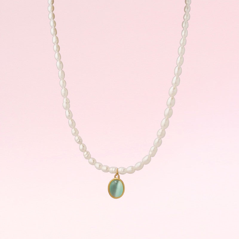 Pearl necklace with a green pendant on a pink background