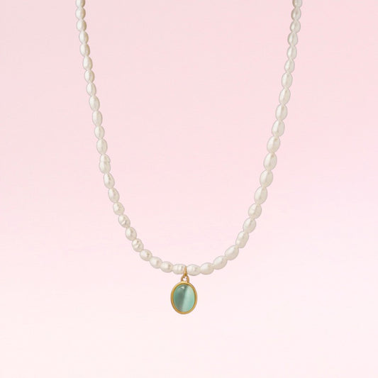 Pearl necklace with a green pendant on a pink background