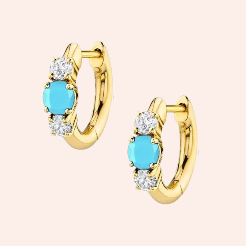 Gold hoop earrings with turquoise stones and clear gemstones on a beige background