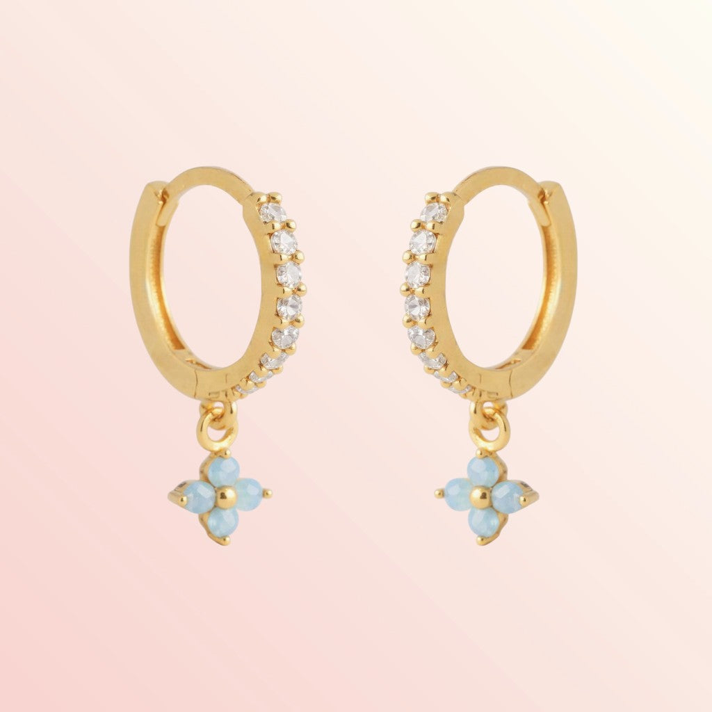 Gold hoop earrings with blue flower charms on a pink background