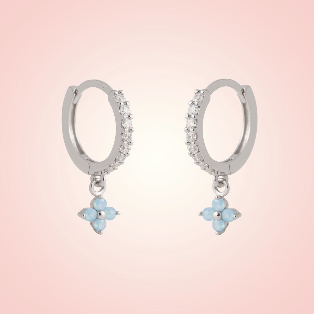 Silver hoop earrings with blue flower charms on a pink background