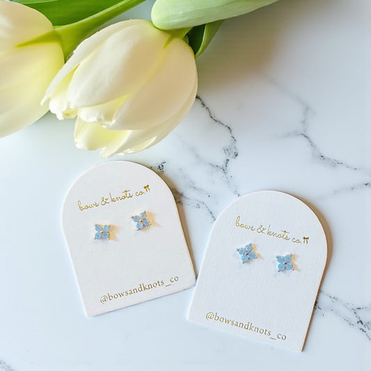 Pair of floral earrings on branded display cards with tulips in the background