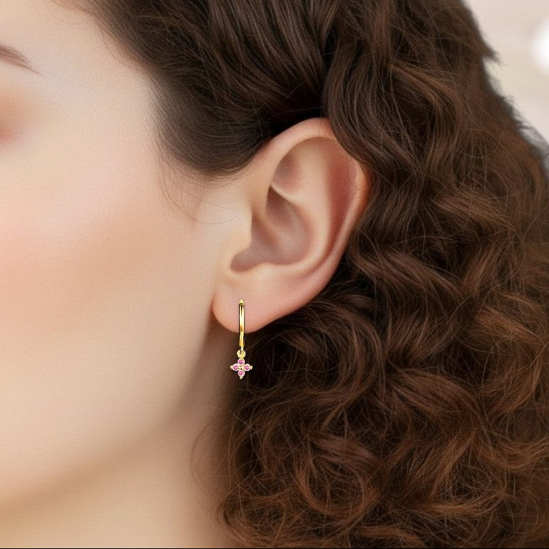 Close-up of an ear wearing a gold earring with a pink gemstone, against a blurred background.