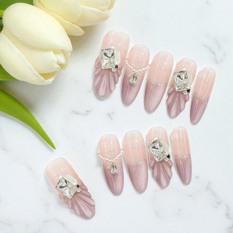 Pink nail art with gemstones on a marble surface with white tulips.