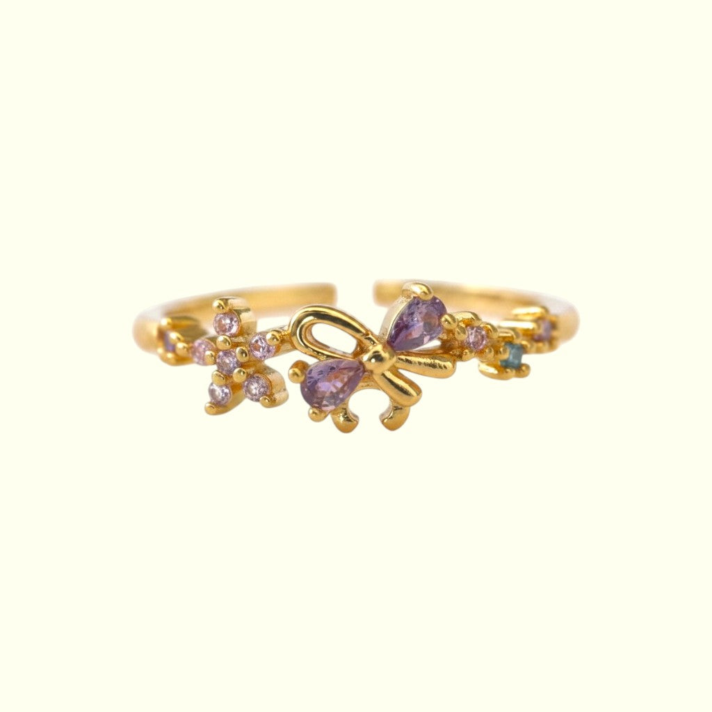 Gold butterfly ring with purple gemstones on a white background