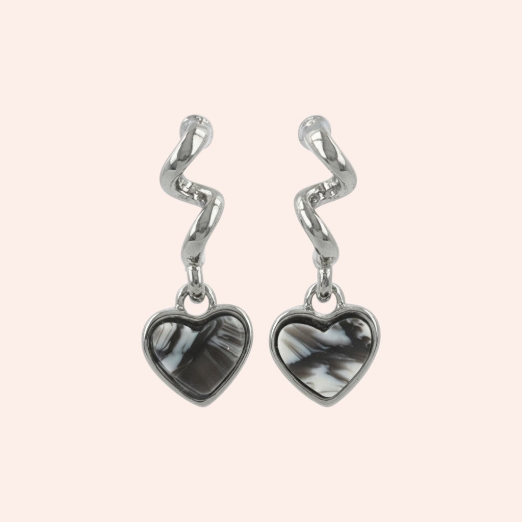 Pair of silver earrings with heart-shaped black stones on a light pink background