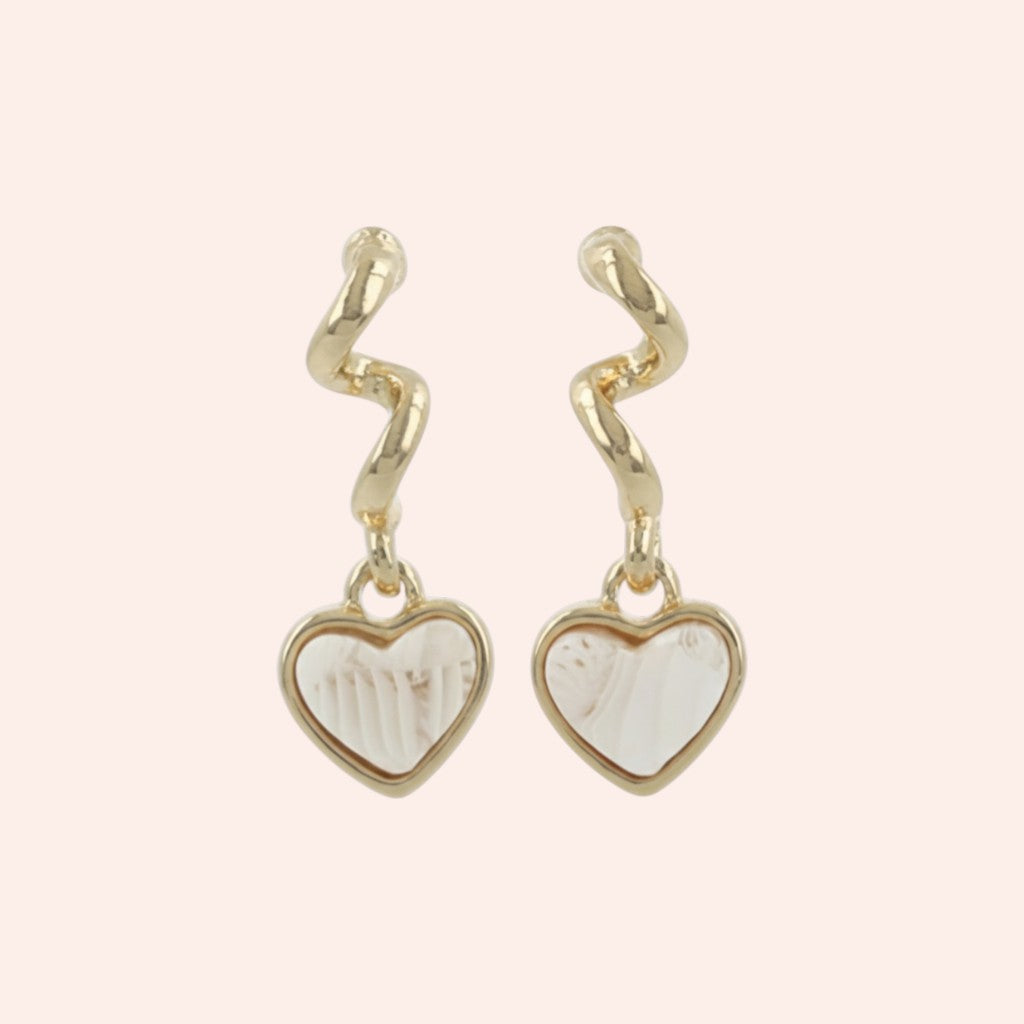 Gold heart-shaped earrings with white centers on a light pink background