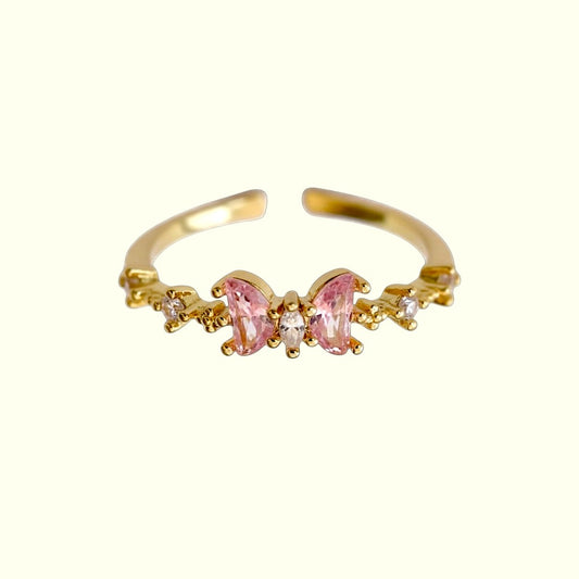 Gold ring with pink butterfly design on a white background
