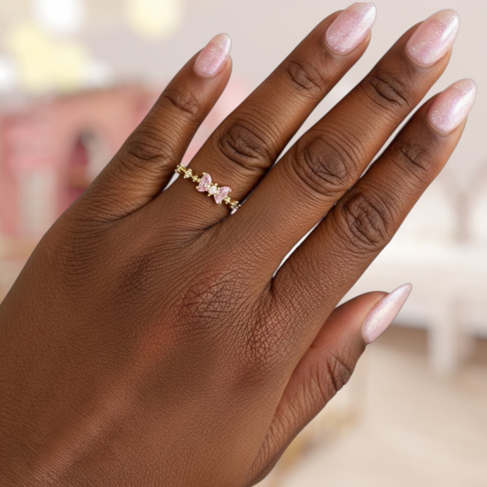 Hand wearing a gold ring with pink gemstones against a blurred background
