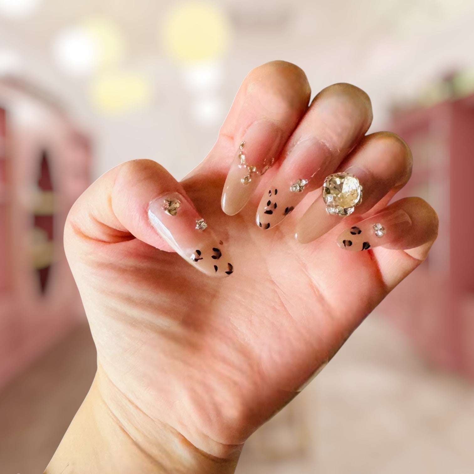 Hand with decorative nails featuring crystals and small stones against a blurred background