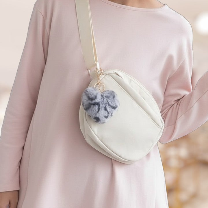 Person wearing a light pink outfit with a white crossbody bag featuring a gray fuzzy pom-pom.