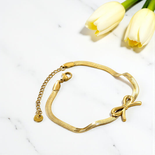 Gold bracelet with bow charm on a white surface with yellow tulips.
