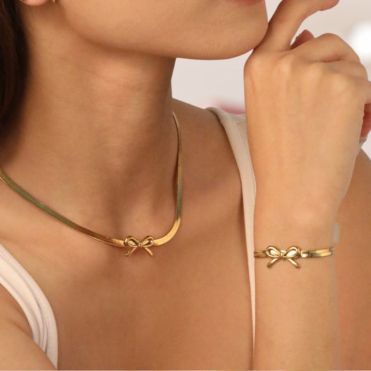 Gold necklace and bracelet with bow design on a person wearing a white top.